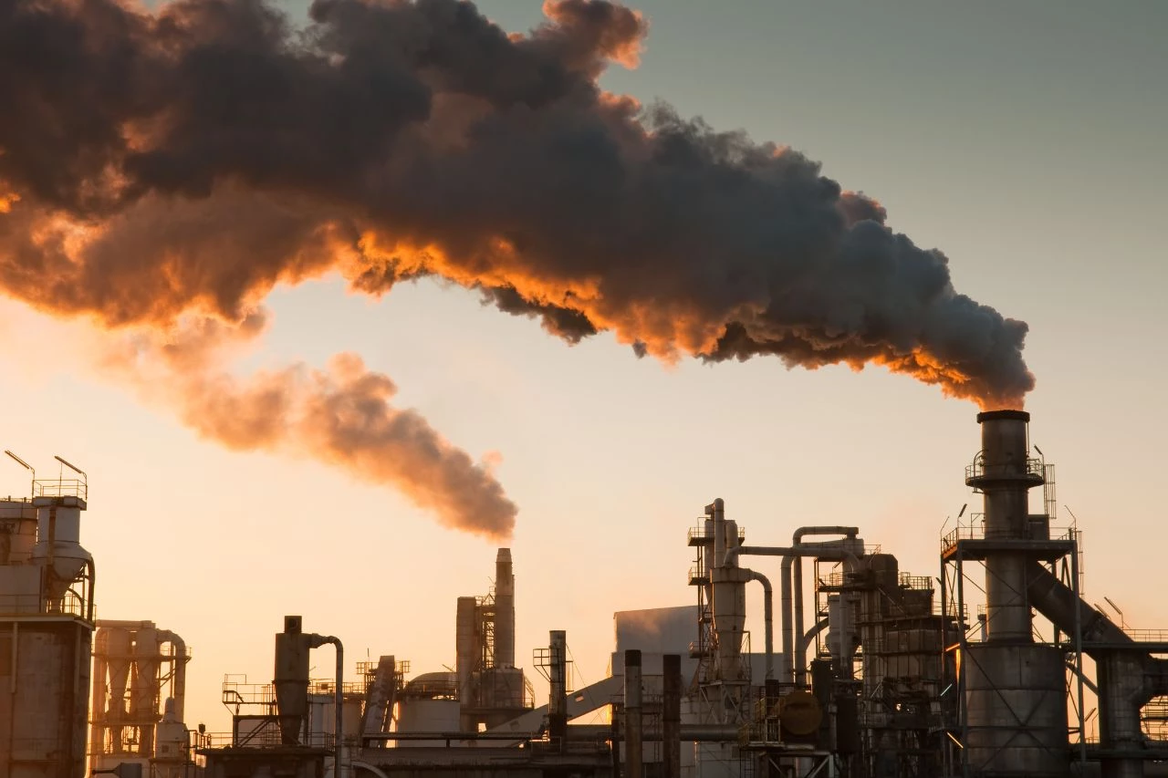 Usine industrielle rejetant une importante fumée dans l’air au coucher du soleil, illustrant les enjeux environnementaux liés à la chaîne d'approvisionnement et à l’évaluation ESG